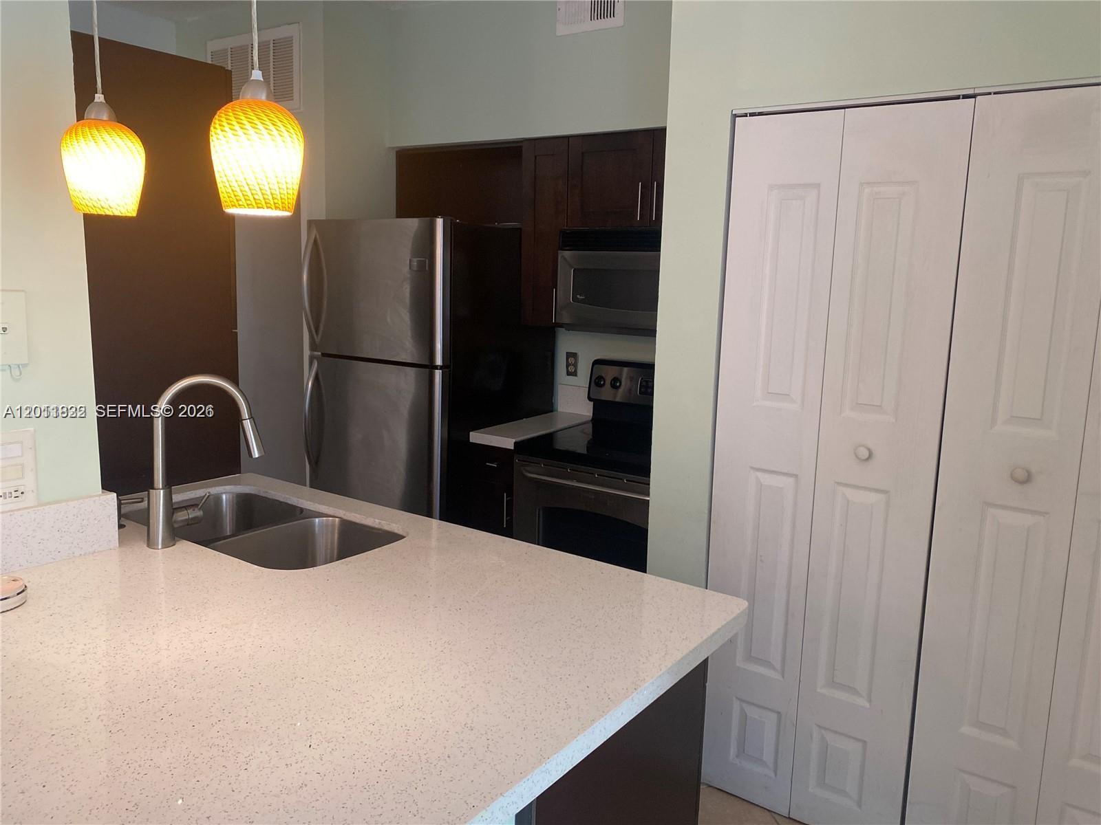 A kitchen features stainless steel appliances, dark wood cabinets, and a white speckled countertop — 18330 NW 68th Ave # G, Hialeah FL 33015, HIALEAH, FL