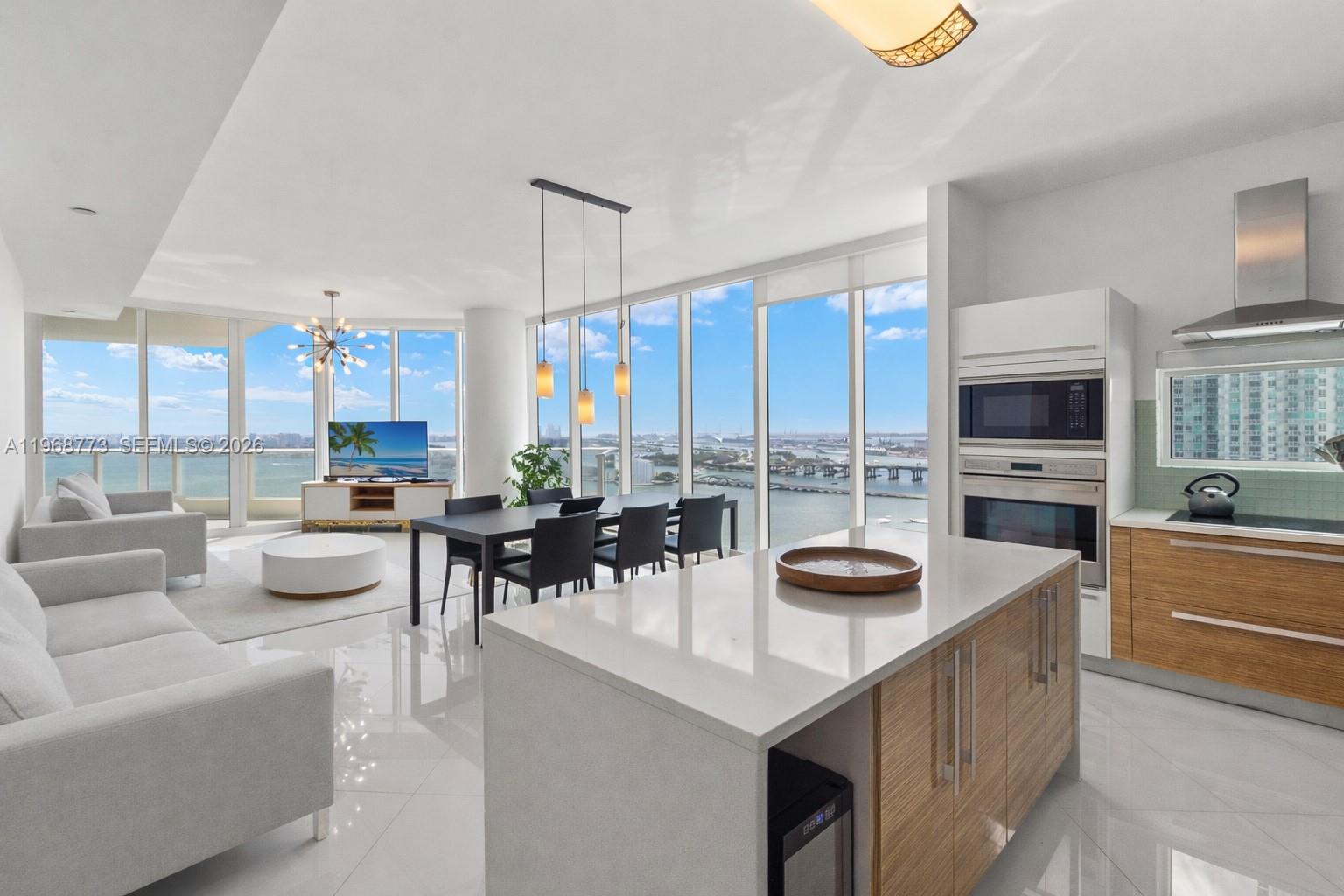 A modern open-concept living and dining area features floor-to-ceiling windows with expansive water views — 2020 N Bayshore Dr # 3102, Miami FL 33137, MIAMI, FL