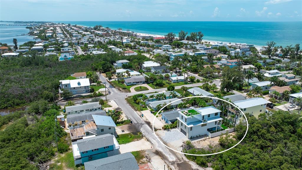An aerial view shows a multi-story white house with a rooftop deck near the coast — 2908 AVENUE B, BRADENTON BEACH, FL