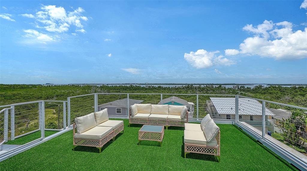 A rooftop deck features artificial turf, outdoor furniture, and a metal railing overlooking a coastal landscape — 2908 AVENUE B, BRADENTON BEACH, FL