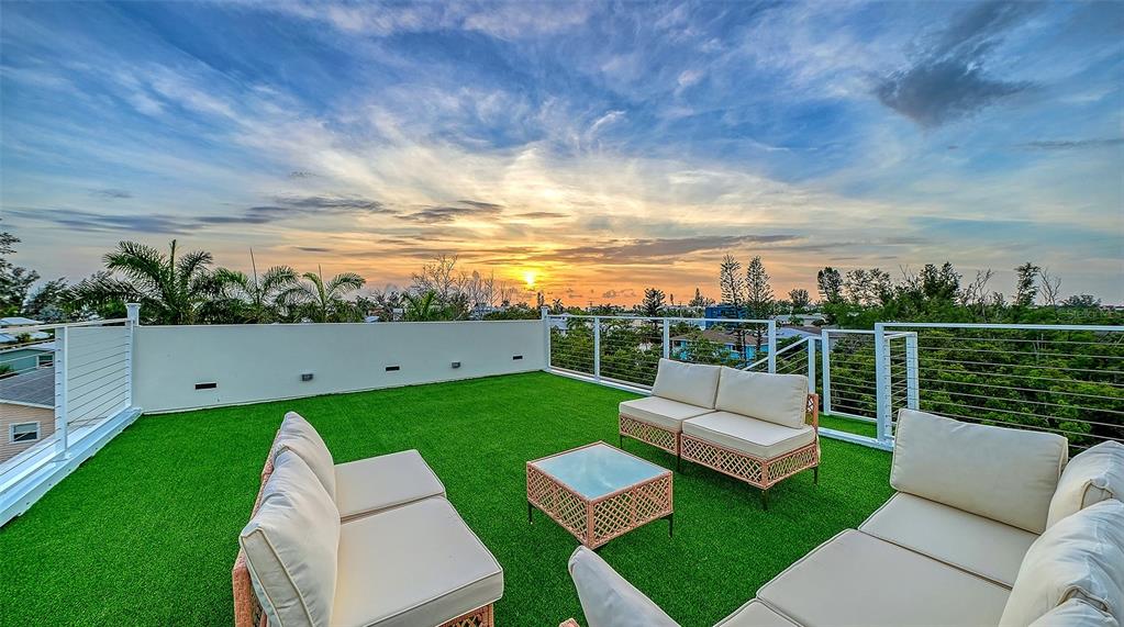 A rooftop terrace features artificial turf, outdoor wicker furniture, and a metal railing at sunset — 2908 AVENUE B, BRADENTON BEACH, FL