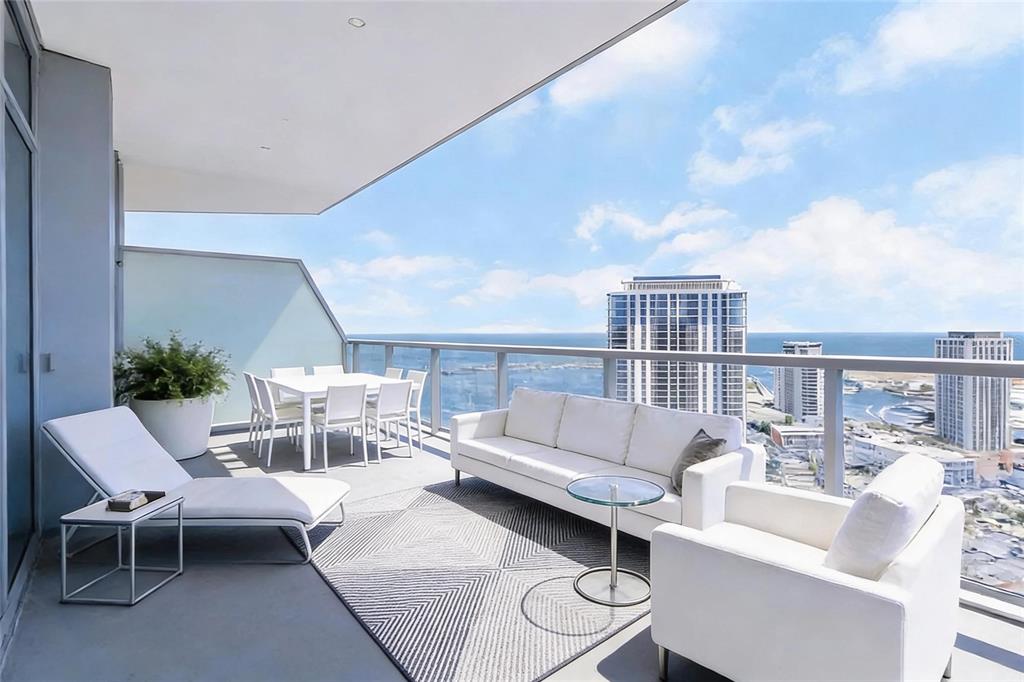A spacious outdoor balcony features white patio furniture, a geometric rug, and panoramic ocean views — 400 CENTRAL AVENUE UNIT 3606, ST PETERSBURG, FL