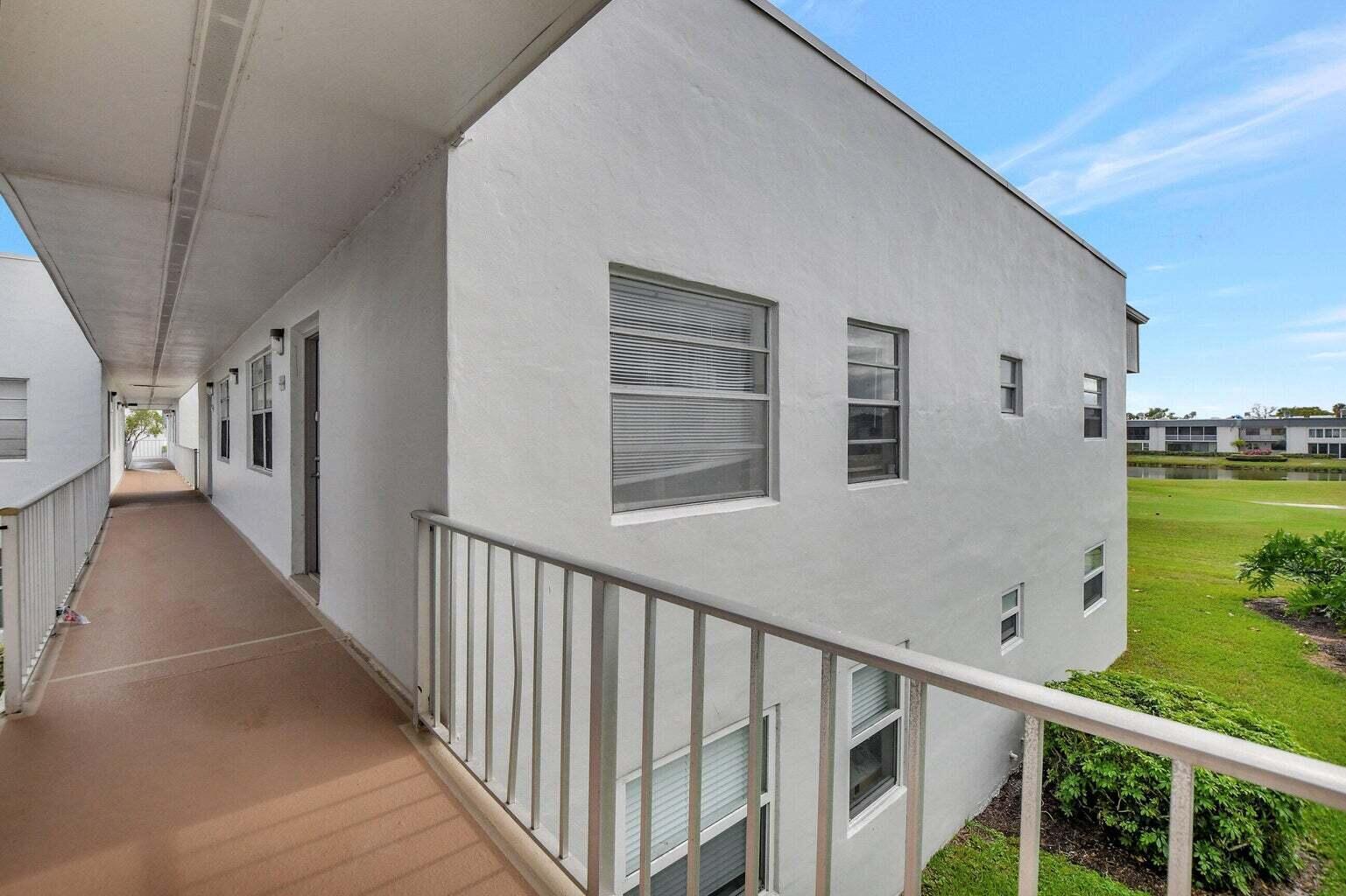 An exterior view of an apartment building walkway with white walls and metal railings — 187 Normandy D, Delray Beach FL 33484, DELRAY BEACH, FL