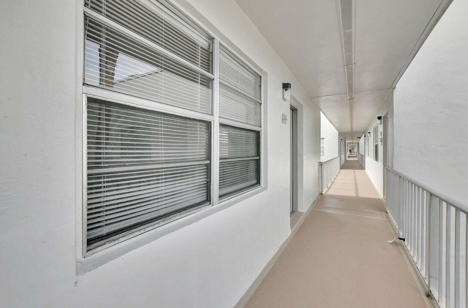 An exterior apartment building hallway with white walls, a beige floor, and metal railings — 187 Normandy D, Delray Beach FL 33484, DELRAY BEACH, FL