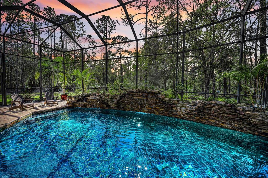 A screened-in swimming pool features a stone waterfall wall and lounge chairs on the deck — 10709 WATULA COURT, NEW PORT RICHEY, FL
