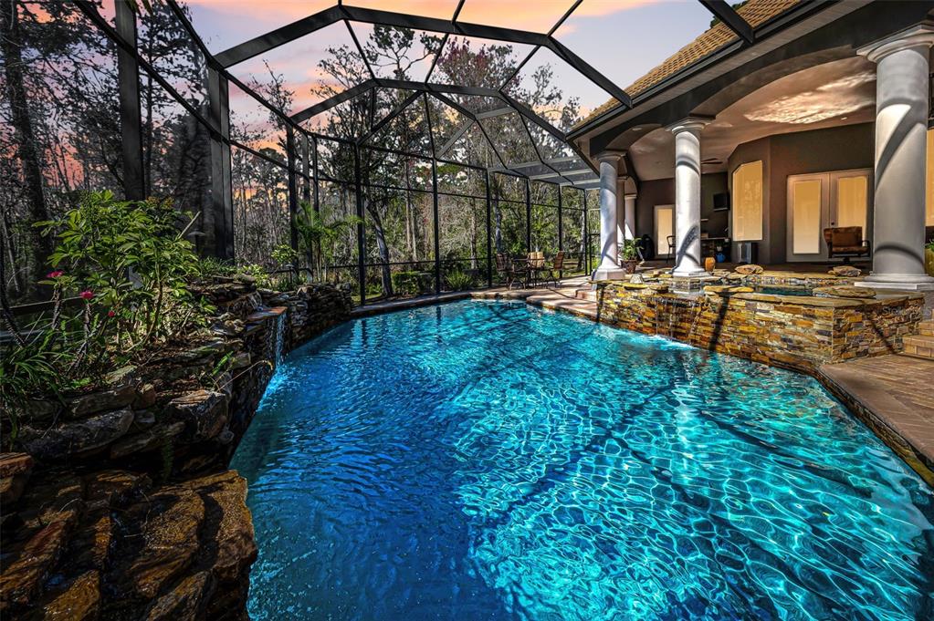 A screened-in swimming pool with a rock waterfall feature and a covered patio area — 10709 WATULA COURT, NEW PORT RICHEY, FL