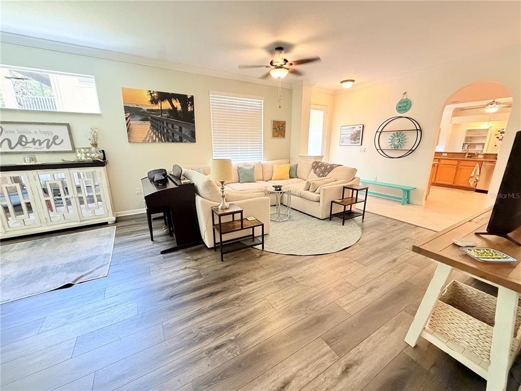 A living room features wood-look flooring, a sectional sofa, a ceiling fan, and an adjacent kitchen — 4244 PRESERVE PLACE, PALM HARBOR, FL