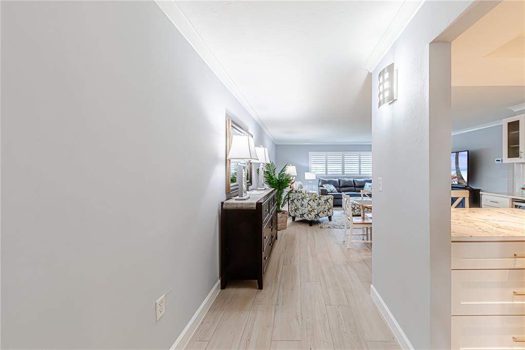 A hallway with light wood-look tile flooring leads into a living room and kitchen area — 616 FLAMINGO DRIVE UNIT 102, VENICE, FL