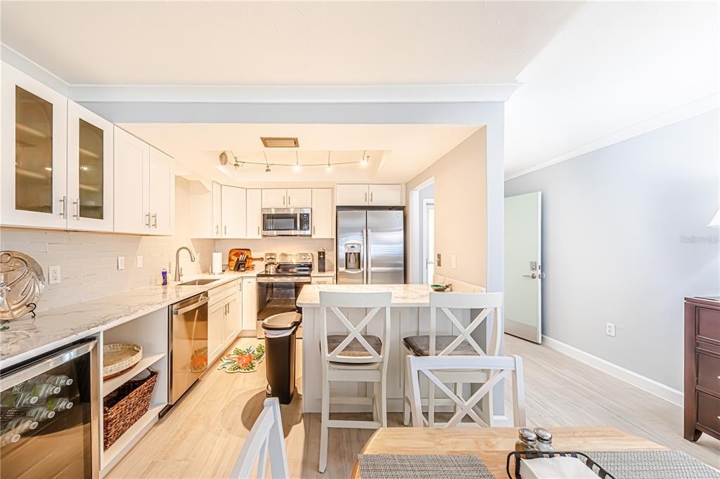 A kitchen features white cabinetry, stainless steel appliances, a breakfast bar, and light wood flooring — 616 FLAMINGO DRIVE UNIT 102, VENICE, FL