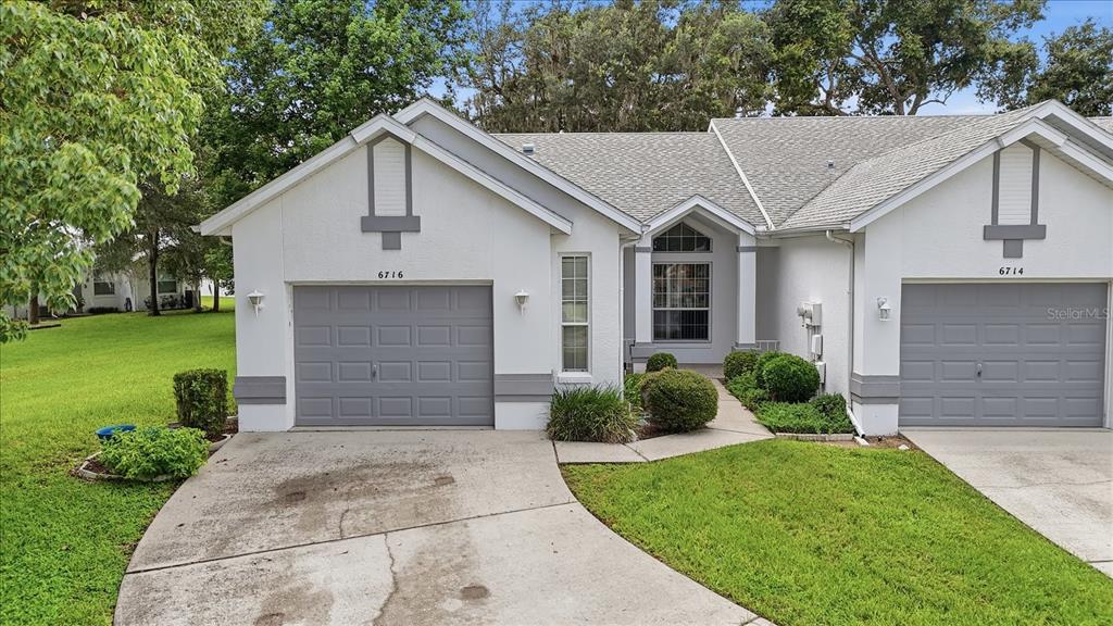 A duplex home exterior features two gray garage doors, white stucco walls, and a shared walkway — 6716 E WAYBRIDGE COURT, INVERNESS, FL
