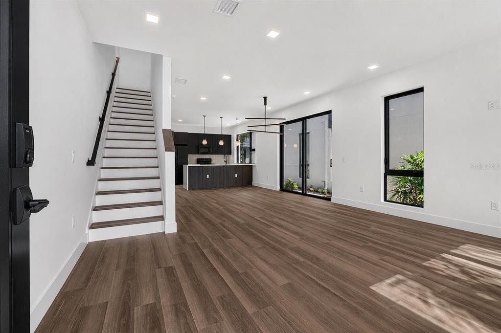 An open-concept living area features wood-look flooring, a staircase, and a modern kitchen — 100 36TH STREET N, ST PETERSBURG, FL