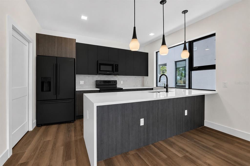A modern kitchen features dark cabinetry, a white quartz island, and black appliances — 100 36TH STREET N, ST PETERSBURG, FL