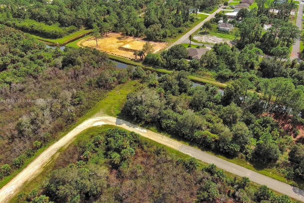 An aerial view shows a cleared dirt lot surrounded by dense trees and a canal — 862 ASHLAND STREET E, LEHIGH ACRES, FL
