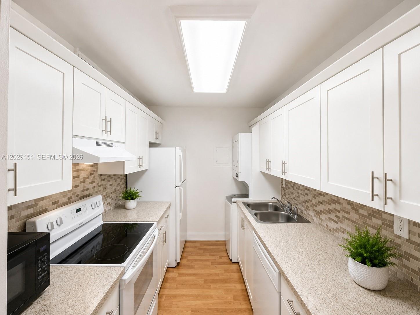 A galley kitchen features white cabinets, light countertops, a tiled backsplash, and stainless steel appliances — MIAMI, FL