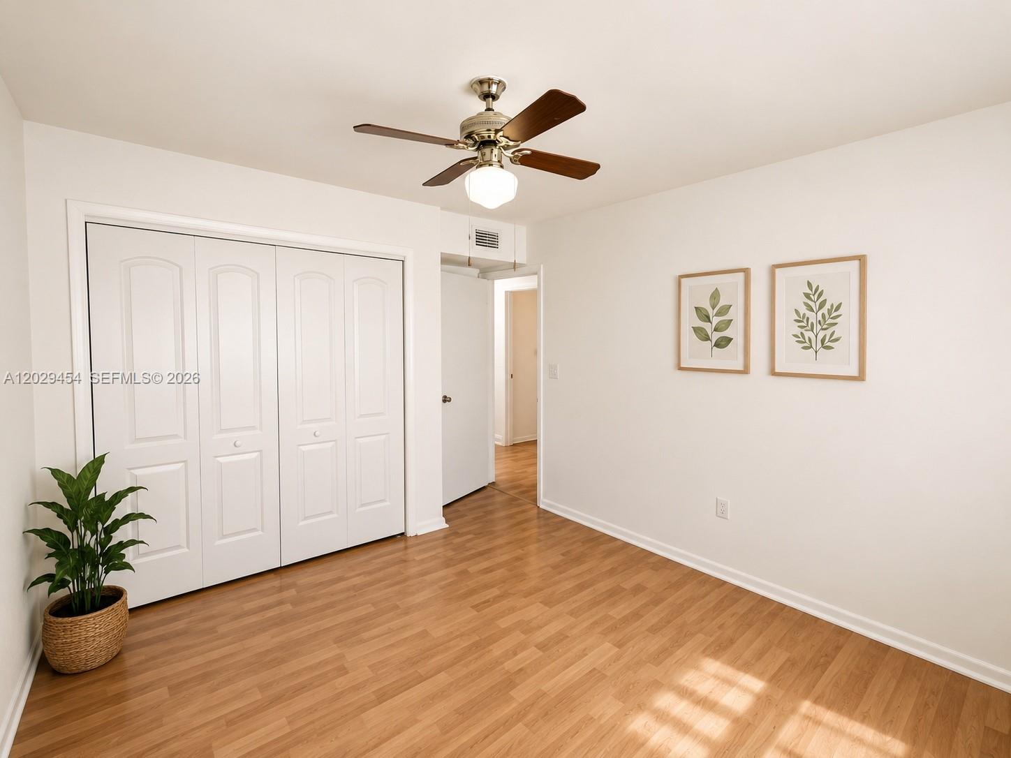 A bedroom features light wood-look flooring, a ceiling fan, white walls, and a closet — MIAMI, FL
