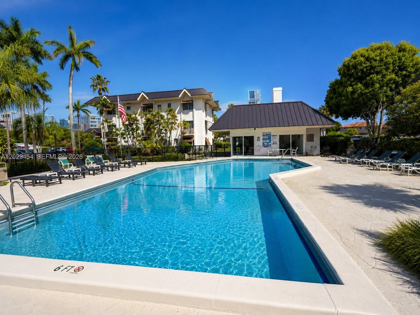 A rectangular swimming pool sits in front of a multi-story building and a clubhouse — MIAMI, FL