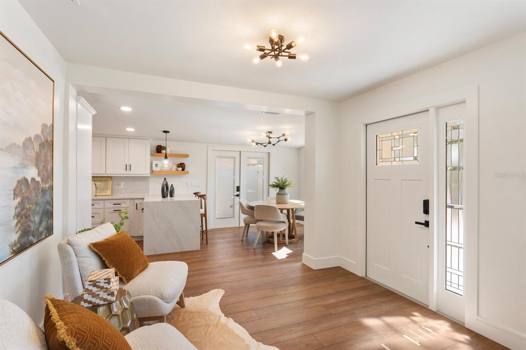 A bright open-concept living area features wood-look flooring, white cabinetry, and a modern entryway door — 3123 W LA SALLE STREET, TAMPA, FL