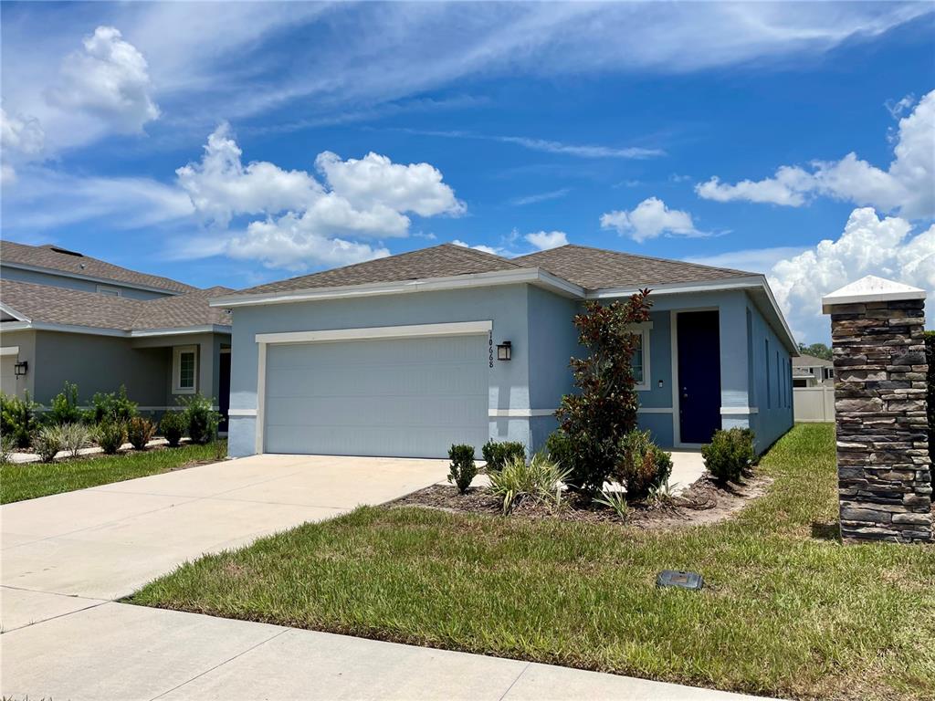 A light blue single-story house features a two-car garage and a dark blue front door — 10668 OLD SYCAMORE LOOP, LAND O LAKES, FL