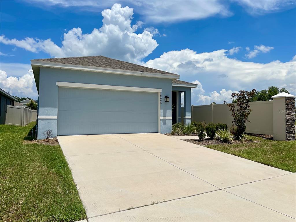 A light blue single-story house features a two-car garage and a concrete driveway — 10668 OLD SYCAMORE LOOP, LAND O LAKES, FL