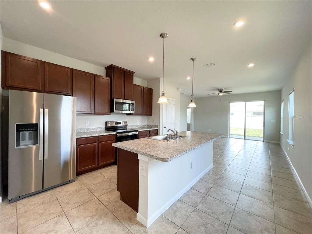 A kitchen features dark wood cabinets, stainless steel appliances, a center island, and tile flooring — 10668 OLD SYCAMORE LOOP, LAND O LAKES, FL
