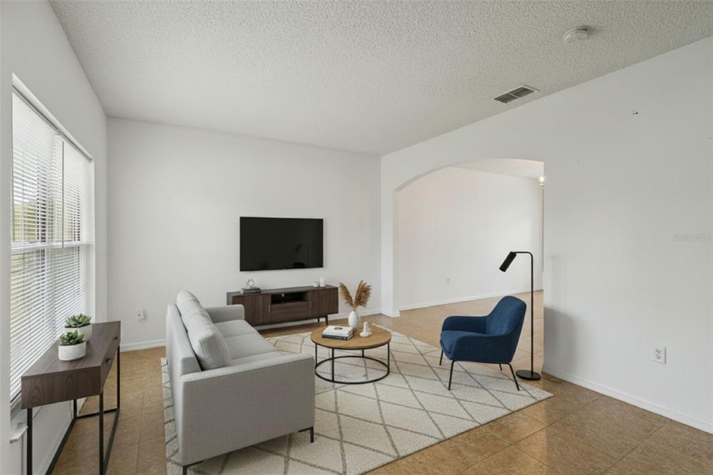 A living room features a grey sofa, a blue armchair, a television, and tile flooring — 342 PUFFER COURT, POINCIANA, FL