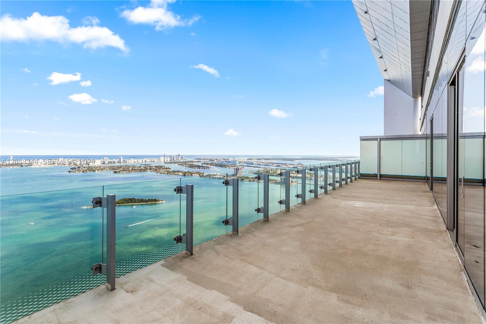 A high-rise balcony features a glass railing overlooking a bay with islands and city views — 700 NE 26th Ter # 01, Miami FL 33137, MIAMI, FL