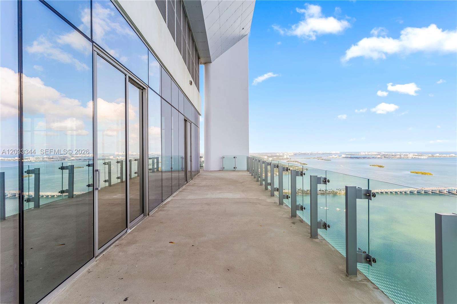 A high-rise balcony features a concrete floor, glass railings, and floor-to-ceiling windows overlooking a bay — 700 NE 26th Ter # 01, Miami FL 33137, MIAMI, FL