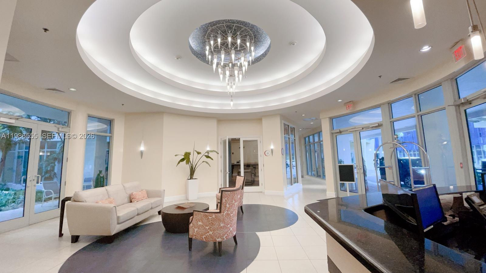 A bright lobby features a circular tray ceiling, a modern chandelier, and a seating area — 1830 Radius Dr # 501, Hollywood FL 33020, HOLLYWOOD, FL