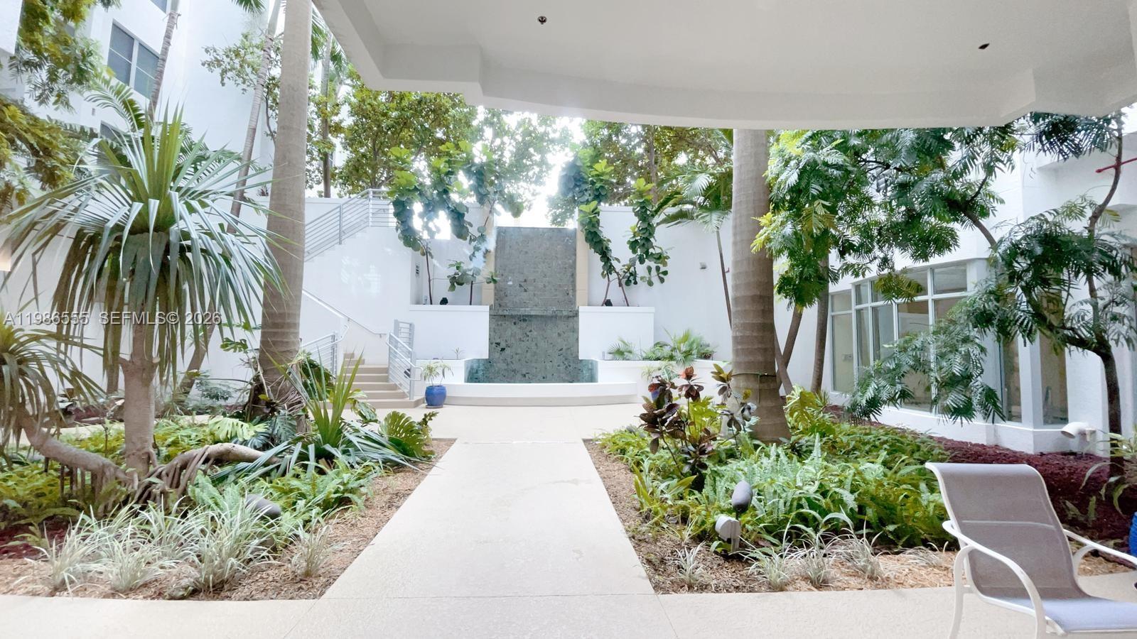 A paved walkway leads through a landscaped courtyard toward a tiered stone water feature — 1830 Radius Dr # 501, Hollywood FL 33020, HOLLYWOOD, FL