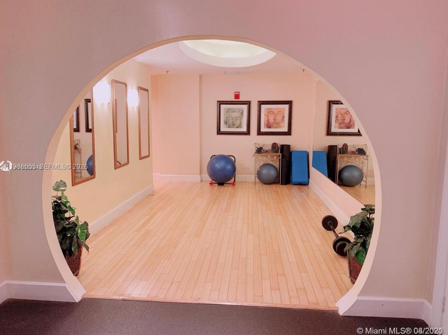 A fitness room with light wood flooring is viewed through a large circular archway — 1830 Radius Dr # 501, Hollywood FL 33020, HOLLYWOOD, FL