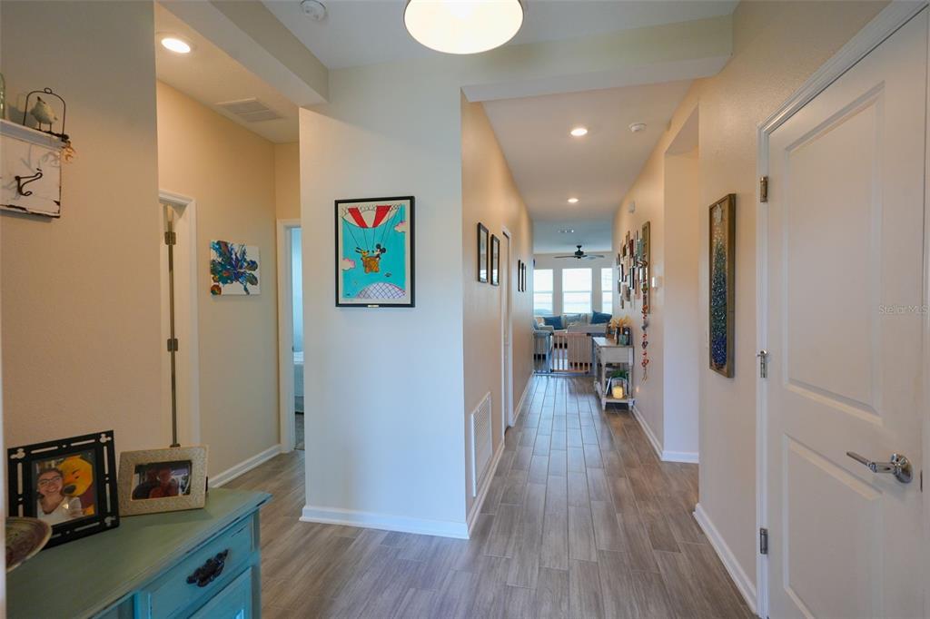A hallway with light wood-look tile flooring leads toward a living area with large windows — 757 CITRUS RESERVE BOULEVARD, DAVENPORT, FL