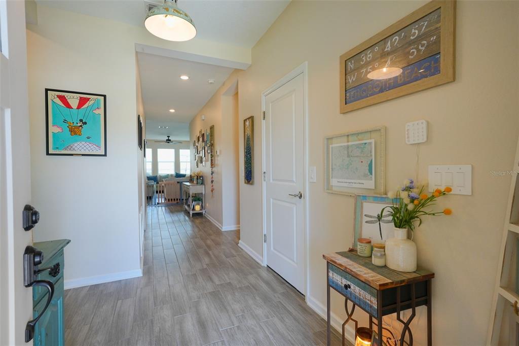A hallway with wood-look tile flooring leads toward a living area with large windows — 757 CITRUS RESERVE BOULEVARD, DAVENPORT, FL