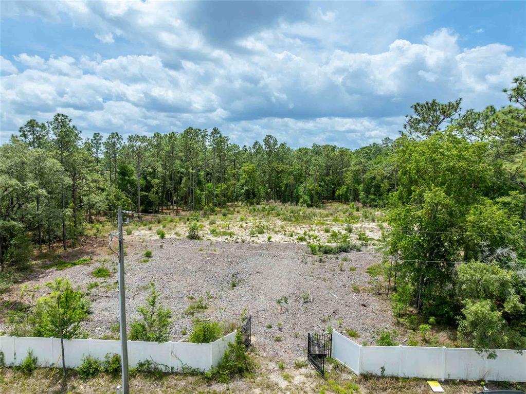 An aerial view shows a cleared, sandy residential lot bordered by trees and a white fence — 15022 GAR STREET, SPRING HILL, FL