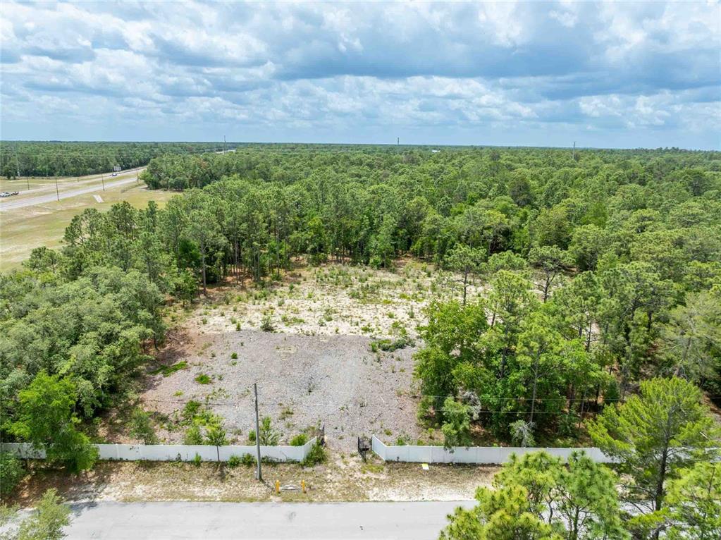 An aerial view shows a cleared, rectangular lot surrounded by dense trees and a fence — 15022 GAR STREET, SPRING HILL, FL