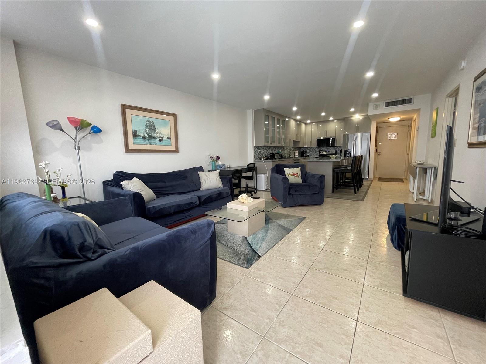 An open-concept living room features blue velvet furniture, tile flooring, and an adjacent kitchen — 3725 S Ocean Dr # 911, Hollywood FL 33019, HOLLYWOOD, FL