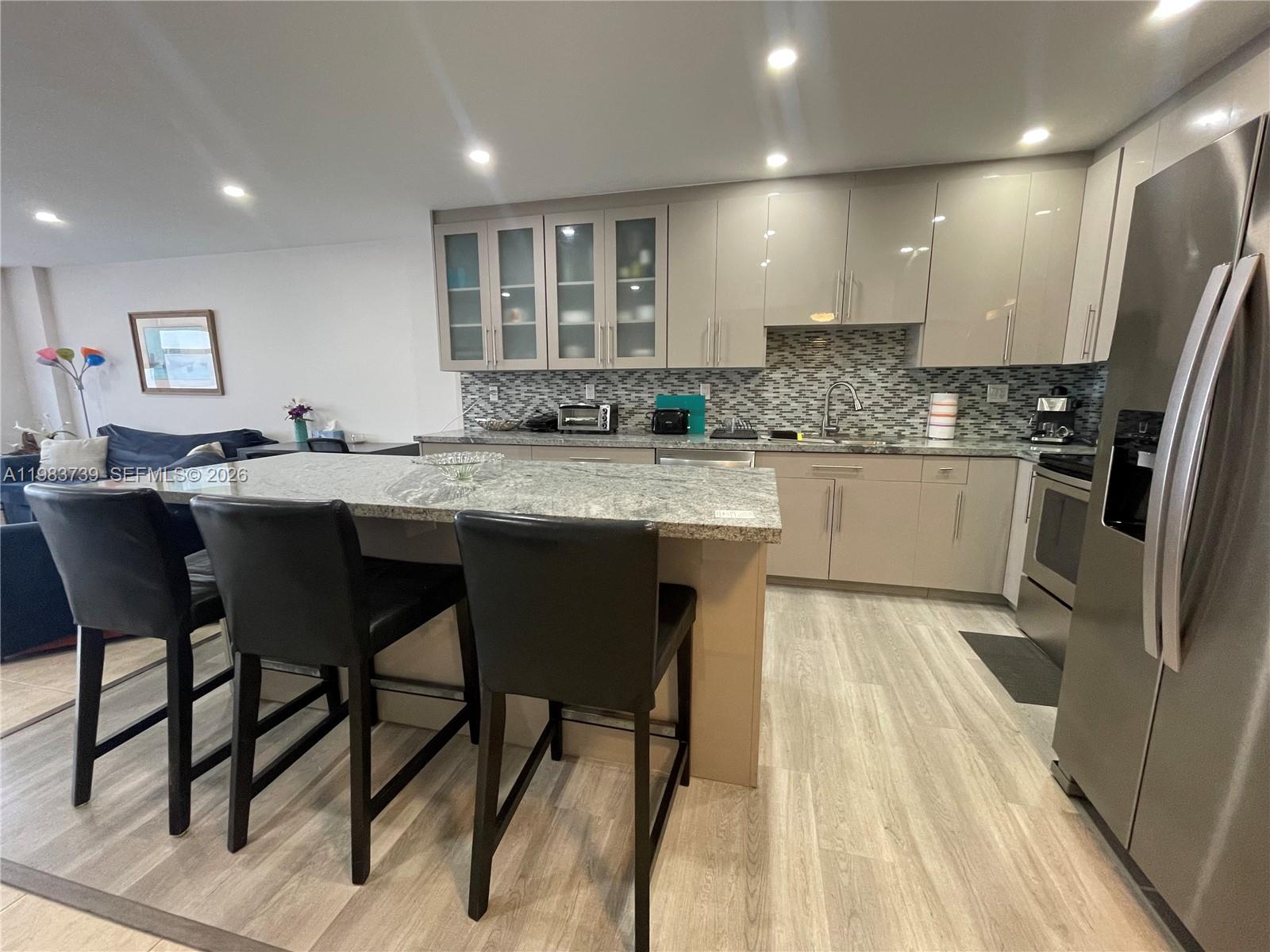 A modern kitchen features light-colored cabinetry, granite countertops, a breakfast bar, and stainless steel appliances — 3725 S Ocean Dr # 911, Hollywood FL 33019, HOLLYWOOD, FL