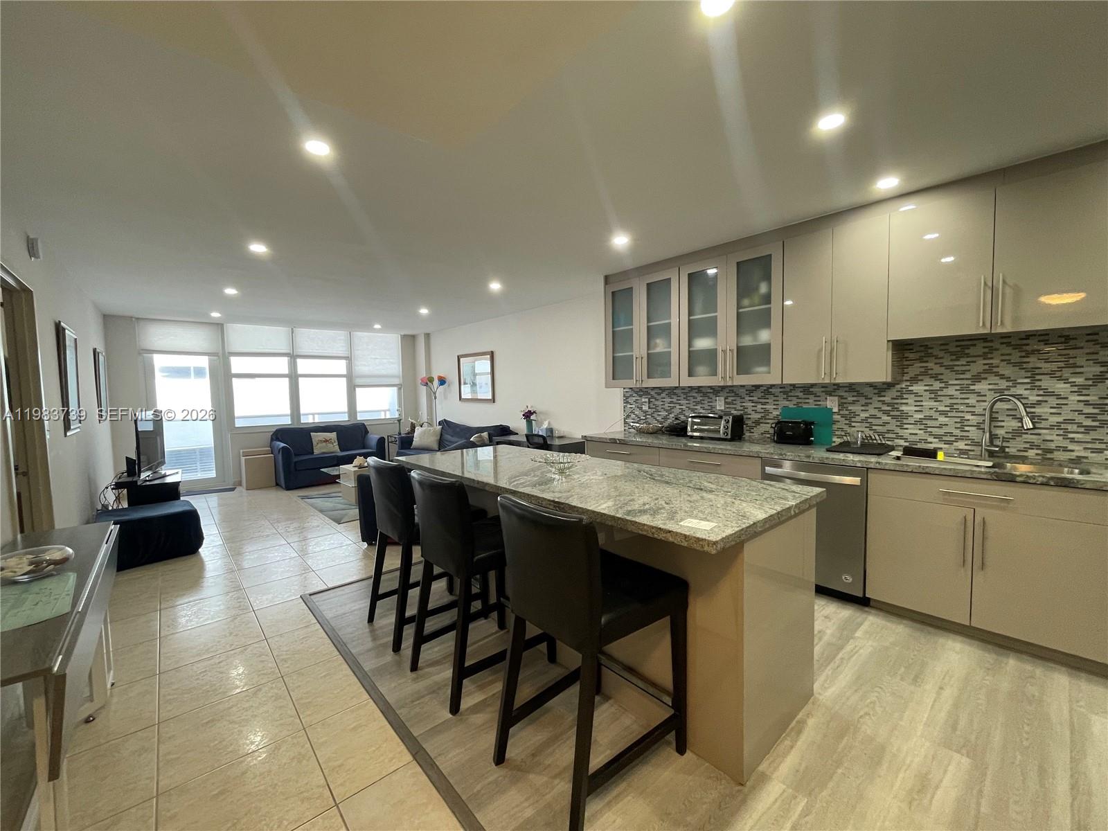 An open-concept kitchen with a granite island and bar stools overlooks a living area — 3725 S Ocean Dr # 911, Hollywood FL 33019, HOLLYWOOD, FL