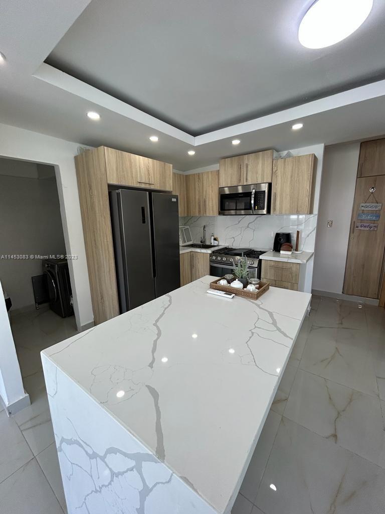 A modern kitchen features light wood cabinetry, a white marble-patterned island, and stainless steel appliances — 2222 Carretera Sanchez # 202, CA 91000, CA