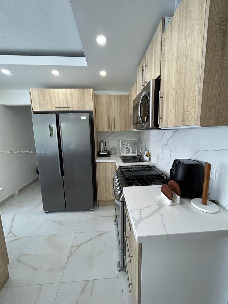 A modern kitchen features light wood cabinets, stainless steel appliances, and white marble-patterned countertops — 2222 Carretera Sanchez # 202, CA 91000, CA