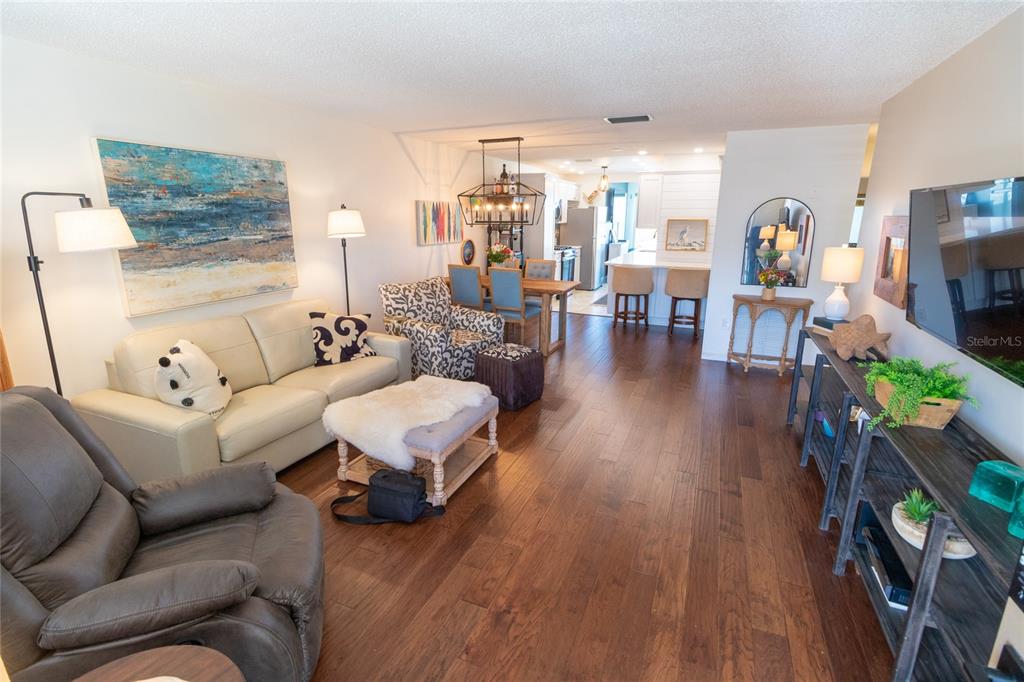A living room with hardwood floors, a beige sofa, a recliner, and an open kitchen — 6075 SHORE BOULEVARD S UNIT 606, GULFPORT, FL