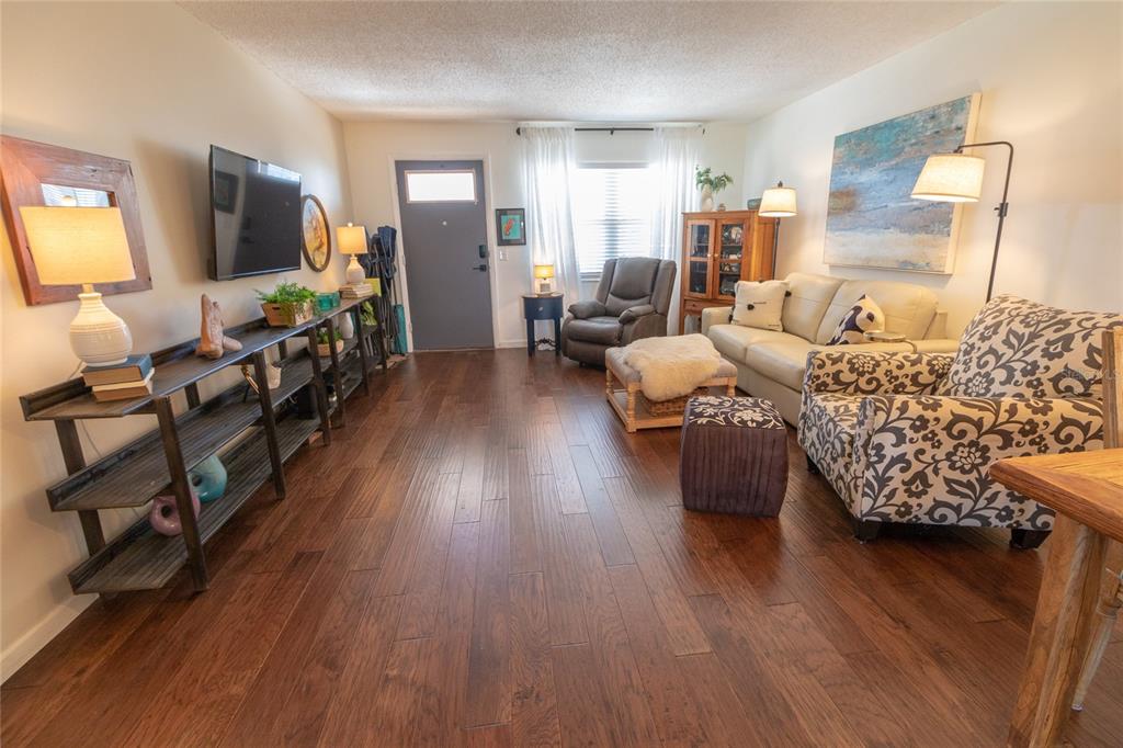 A living room features dark wood flooring, a television, a sofa, and an armchair — 6075 SHORE BOULEVARD S UNIT 606, GULFPORT, FL