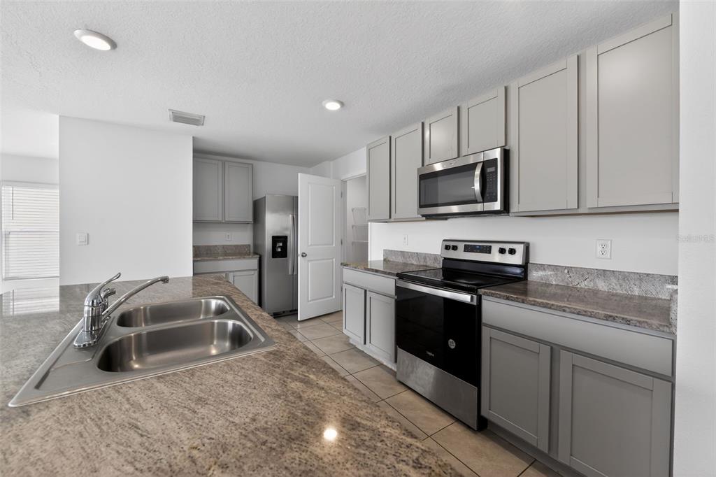 A kitchen features gray cabinets, granite countertops, stainless steel appliances, and a double-basin sink — 439 SUNLIT CORAL STREET, RUSKIN, FL