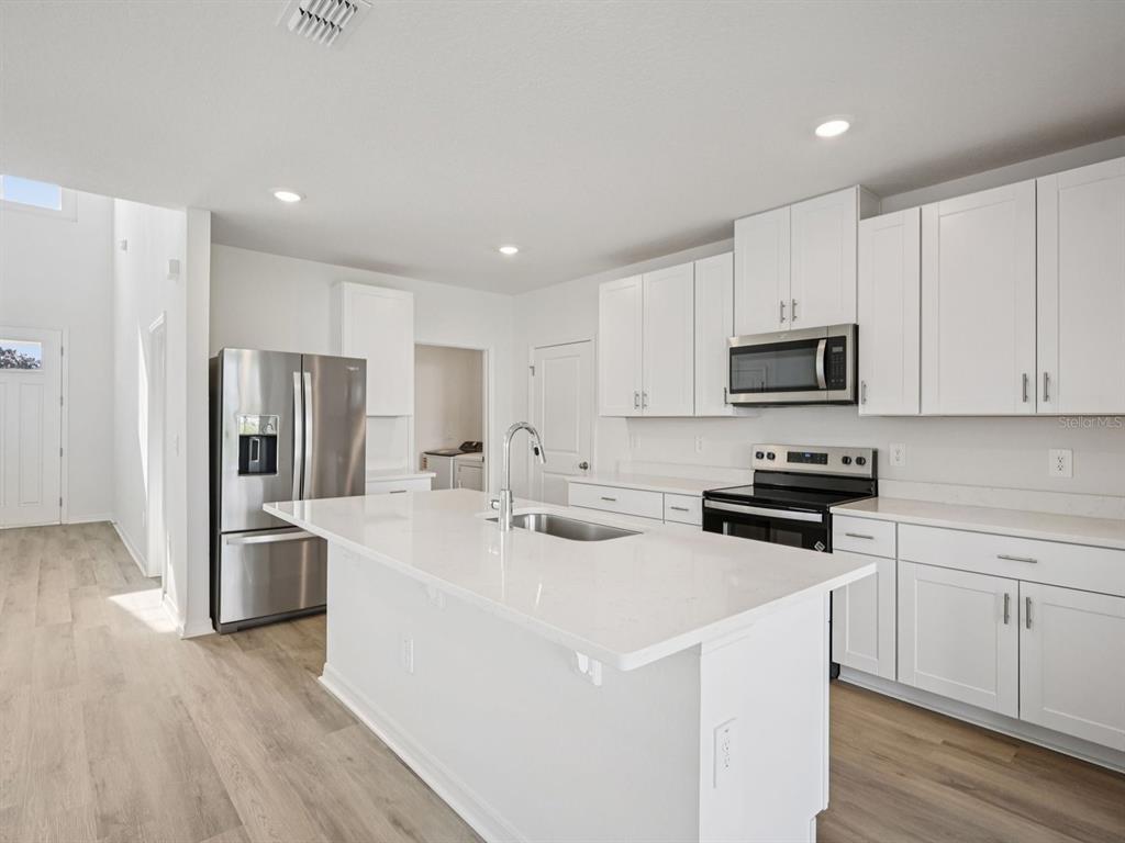 A modern kitchen features white cabinets, stainless steel appliances, and a large quartz-topped island — 7930 LAKE POWELL PLACE, PARRISH, FL