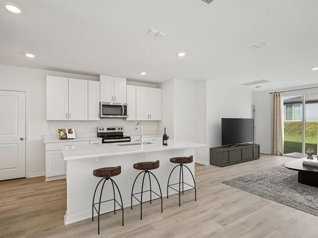 A modern kitchen with white cabinets, a quartz island, and bar stools opens to a living area — 7930 LAKE POWELL PLACE, PARRISH, FL