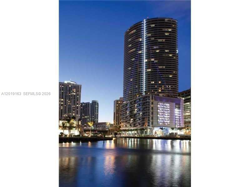 A tall, cylindrical skyscraper stands illuminated at dusk beside a body of water — 200 Biscayne Boulevard Way # 4904, Miami FL 33131, MIAMI, FL