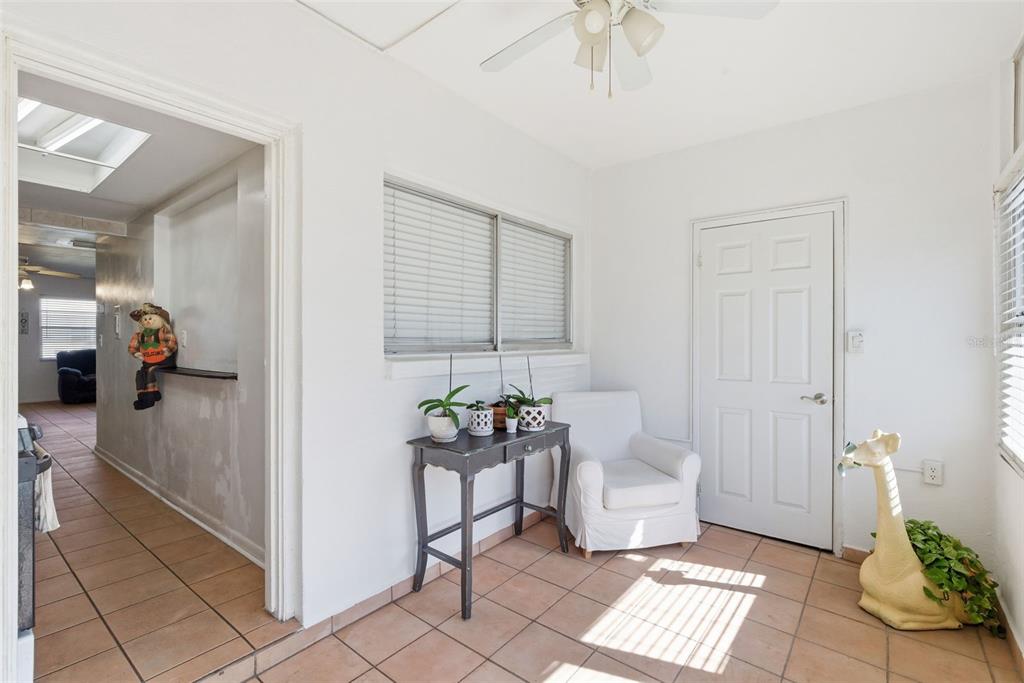 A sunroom with tile flooring, a white armchair, a console table, and a white door — 5876 21ST STREET N UNIT 5, ST PETERSBURG, FL