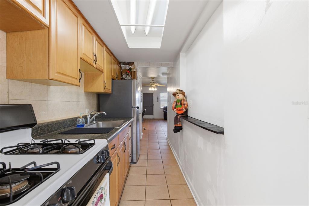 A narrow galley kitchen features wood cabinets, a gas stove, and a tiled floor — 5876 21ST STREET N UNIT 5, ST PETERSBURG, FL