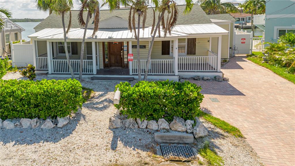 A light yellow house with a white porch and metal roof sits behind a hedge — 16029 REDINGTON DRIVE, REDINGTON BEACH, FL