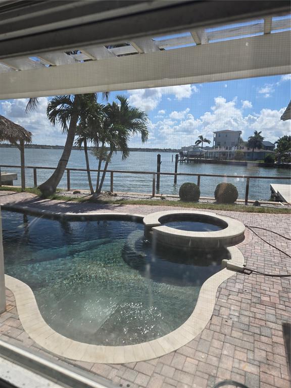 A swimming pool and spa overlook a waterfront view with palm trees and a dock — 16029 REDINGTON DRIVE, REDINGTON BEACH, FL