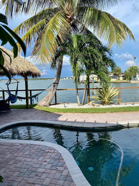 A swimming pool sits on a brick patio overlooking a bay with palm trees — 16029 REDINGTON DRIVE, REDINGTON BEACH, FL